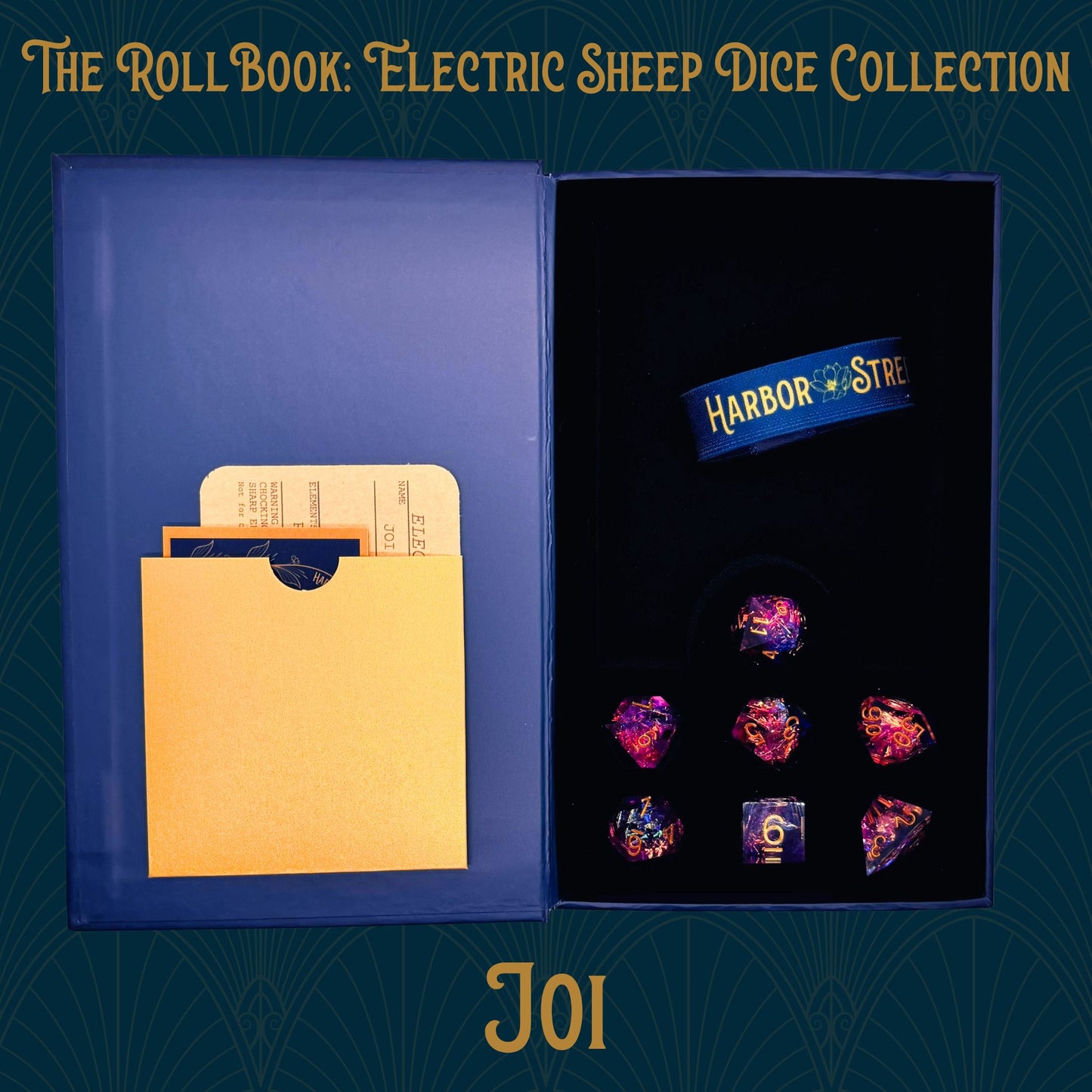 Open blue book box with Joi seven polyhedral dice collection. Blue elastic band with the harbor street logo. Gold paper pocket