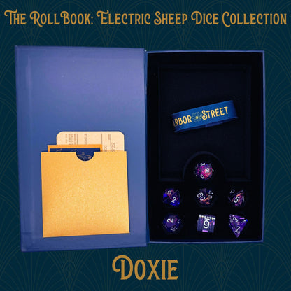 Blue book box with Doxie seven polyhedral dice collection. Blue elastic band with the Harbor Street logo. Gold paper pocket