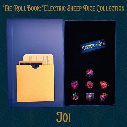 Open blue book box with Joi seven polyhedral dice collection. Blue elastic band with the harbor street logo. Gold paper pocket
