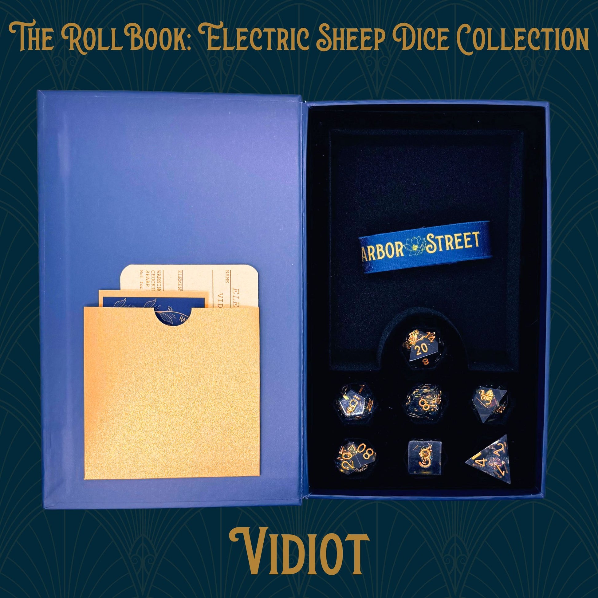  Open blue book box with vidiot seven polyhedral dice collection. Blue elastic band with the harbor street logo. Gold paper pocket
