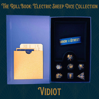  Open blue book box with vidiot seven polyhedral dice collection. Blue elastic band with the harbor street logo. Gold paper pocket
